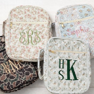 May include: Four quilted cosmetic bags with various patterns and embroidered details. One bag has a camouflage design, another a floral pattern with the letter "R", and a third has the name "Sophie". The fourth bag features a duck pattern with the letters "HSK".