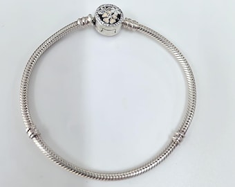 May include: A silver bracelet with a snake chain design. The bracelet features a round charm with a floral design in black, white, and cream colors. The charm is encrusted with small, clear stones.