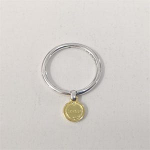 May include: A silver ring with a small, round, gold-coloured charm. The charm is inscribed with the word "Love" in a delicate font. The ring is set against a plain white background.