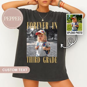 Może przedstawiać: Czarny t-shirt ze zdjęciem dziecka z plecakiem i czapką. Koszulka ma złoty napis "FOREVER IN THIRD GRADE". Mniejsze zdjęcie znajduje się po prawej stronie z napisem "UPLOAD PHOTO".