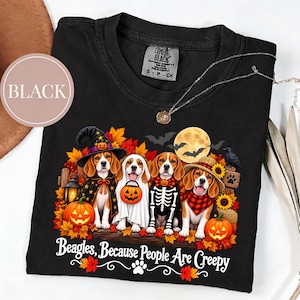 Może przedstawiać: Czarny t-shirt z grafiką przedstawiającą cztery psy rasy beagle w kostiumach na Halloween, w tym czarownicę, ducha, szkielet i stracha na wróble. Wzór zawiera dynie, jesienne liście, pełnię księżyca oraz napis Beagles, Because People Are Creepy.