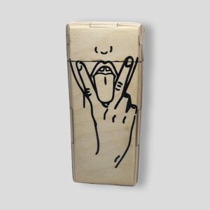 May include: A light-colored wooden box with a black graphic of a hand making a peace sign with the tongue sticking out. The box has a rectangular shape with a hinged lid.