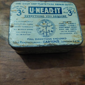 May include: A vintage U-NEAD-IT motorcycle tyre repair kit in a rectangular tin. The tin is off-white with blue text and graphics, including a clock design. Text on the tin includes "Everything You Require" and "Full Directions Enclosed."
