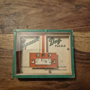 May include: Vintage "Speech Day Puzzle" game in a green-framed box. The game features a clear plastic cover, with the words "Speech" and "Day" on the top. The puzzle includes a platform with a table and chairs, and small metal balls.
