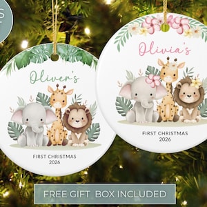 Op de afbeelding: Twee ronde witte keramische ornamenten met aquarelillustraties van een babyolifant, giraf en leeuw omringd door tropische bladeren. Het linker ornament zegt Oliver's, het rechter zegt Olivia's, en beide bevatten de tekst FIRST CHRISTMAS 2026.