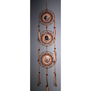 May include: A vertical wall hanging featuring three circular frames connected by chains. Each frame contains a round ceramic disc with a central illustration of a wolf, a bear, and an eagle. The structure is wrapped in tan cord with hanging feathers.