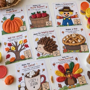 May include: A set of eight educational activity mats for play dough featuring autumn themes like a pumpkin, apple basket, scarecrow, tree with leaves, hedgehog, pie, hot cocoa, and turkey, accompanied by several colourful play dough containers.