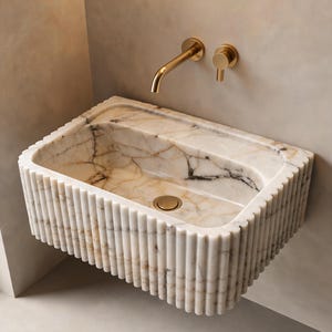 Puede incluir: Un lavabo rectangular de mármol con exterior estriado y desagüe dorado. El interior del lavabo tiene vetas marrones y negras. Un grifo y un control de agua dorados están montados en la pared sobre el lavabo.