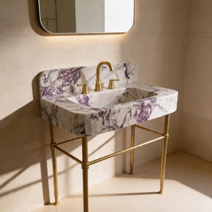 May include: A marble sink with a white base and purple veining, set on a gold-colored metal stand. The sink has a gold faucet and fixtures. A mirror is above the sink.