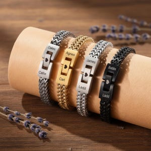 May include: Four personalized bracelets with names engraved on the clasps. The bracelets are silver, gold, and black, with a woven chain design. Each clasp features a heart symbol. The names include "Callie", "Oakes", "Agnes", "Carl", "James", "Ladd", and "Babbs".