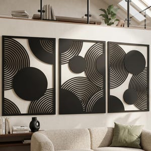 Pode incluir: Conjunto de três painéis de arte de parede pretos. Cada painel apresenta um design geométrico com círculos concêntricos e formas circulares pretas sólidas. Os painéis são emoldurados em preto e montados em um fundo branco, criando uma estética moderna.