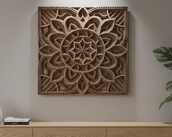 Puede incluir: Una pieza de arte mural de madera en capas con un diseño de mandala, que presenta intrincados patrones recortados en tonos marrones. La obra de arte es cuadrada y cuelga sobre un mueble de madera de color claro. También se ven una gran planta en maceta y jarrones decorativos.