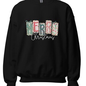 May include: Black sweatshirt with a festive design. The design features the word "MERRY" spelled out with decorative gift boxes in green, red, and white. Below the word "MERRY" is the word "Christmas" in a cursive font.