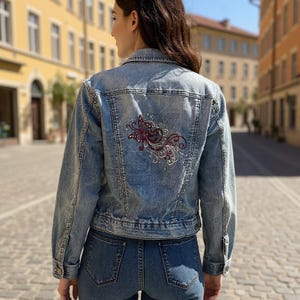 May include: Light blue denim jacket with a decorative embroidered butterfly design on the back. The jacket has a classic fit with button closures and pockets. The model is wearing blue jeans.