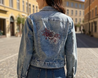 May include: Light blue denim jacket with a decorative embroidered butterfly design on the back. The jacket has a classic fit with button closures and pockets. The model is wearing blue jeans.