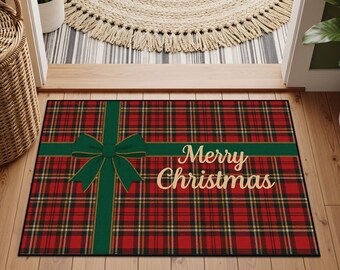 Puede incluir: Una alfombra de puerta navideña rectangular con un patrón de cuadros rojos y negros. Un diseño de cinta y lazo verde cruza la alfombra, con las palabras "Merry Christmas" en letras doradas. La alfombra está sobre un suelo de madera.