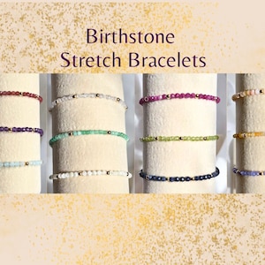 May include: Image of several birthstone stretch bracelets. The bracelets are displayed on cylindrical forms. Each bracelet is made of small, colorful beads. The text "Birthstone Stretch Bracelets" is at the top of the image.