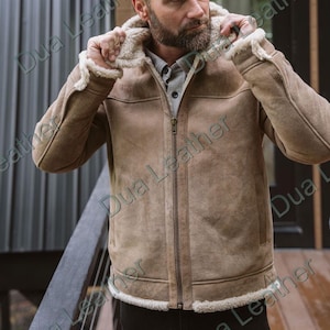 May include: A tan leather jacket with a hood and a full-length zip. The jacket features a shearling lining and trim. The person in the image is wearing the jacket. The jacket has two front pockets.