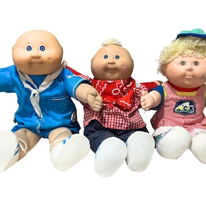 May include: Three Cabbage Patch Kids dolls with soft bodies and vinyl heads. The left doll wears a blue sailor outfit. The center doll wears a red and white checkered shirt with a red bandana. The right doll has blonde hair and striped overalls.
