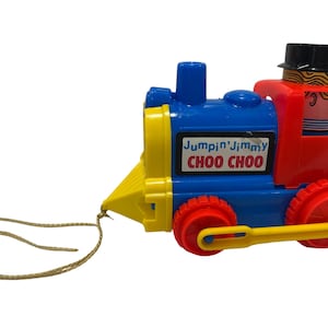 May include: A colorful toy train with the text "Jumpin' Jimmy Choo Choo." The train is primarily blue, red, and yellow, with red wheels and a yellow handle. A string is attached for pulling.
