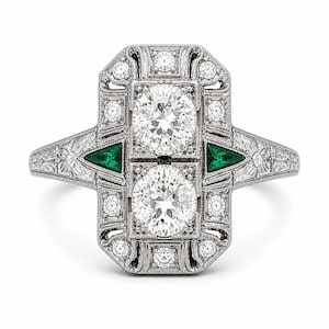 Art Deco diamond engagement ring with geometric halo design, emerald green triangular accents, and intricate vintage inspired milgrain detailing throughout.
