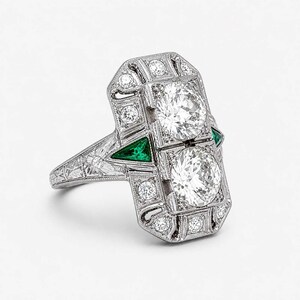 Vintage inspired geometric ring with white diamonds, emerald green accents, engraved shoulders, and detailed milgrain craftsmanship in Art Deco style.