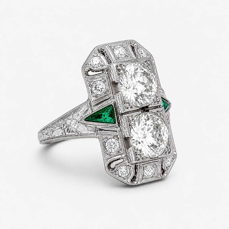 Vintage inspired geometric ring with white diamonds, emerald green accents, engraved shoulders, and detailed milgrain craftsmanship in Art Deco style.