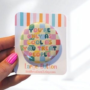 May include: A large, round button with the text "YOU'RE ONLY AS COOL AS YOU TREAT PEOPLE" in colorful letters. The button has a checkered background in pastel colors. The button is on a white card with the words "Large Button" and a website address.