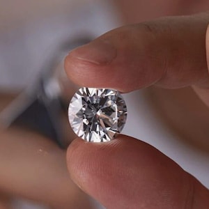 May include: A sparkling, round-cut diamond held between fingers. The gemstone's facets catch the light, creating a brilliant display. The background is out of focus, highlighting the diamond. This image showcases a precious jewel, a symbol of wealth.