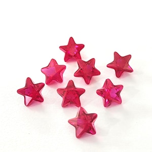 May include: A collection of eight faceted, star-shaped beads in a vibrant shade of red. The beads are arranged on a white surface, showcasing their sparkling, jewel-like appearance. These decorative beads are ideal for jewelry making or craft projects.