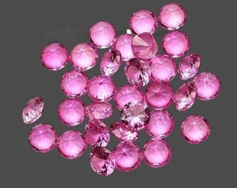 Puede incluir: Un conjunto de gemas rosas facetadas dispersas sobre un fondo gris. Las gemas, de varios tamaños, presentan un tallado brillante que refleja la luz. El efecto general es de brillo y lujo, lo que sugiere joyería o elementos decorativos.