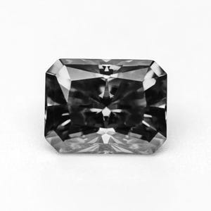Op de afbeelding: Een grijskleurige diamant met een radiant-slijpvorm en een rechthoekige vorm. De edelsteen heeft meerdere facetten die het licht reflecteren, waardoor een sprankelend effect ontstaat. De diamant staat tegen een witte achtergrond, wat de helderheid en schittering benadrukt.