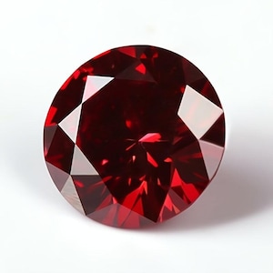 Puede incluir: Una gema facetada, de corte redondo, de color rojo intenso. La gema tiene múltiples facetas que reflejan la luz, creando un brillo brillante. La piedra preciosa se presenta sobre un fondo blanco liso, resaltando su color y claridad.