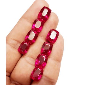 Può includere: Primo piano di otto pietre preziose rosse scuro, sfaccettate e di forma ovale. Le gemme sono disposte in due file verticali, ciascuna con quattro pietre. Le pietre hanno un alto grado di chiarezza e brillantezza.
