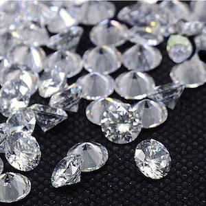Puede incluir: Una colección de diamantes claros y facetados dispersos sobre una superficie oscura. Los diamantes varían en tamaño y forma, reflejando la luz y creando un efecto brillante. La imagen muestra el brillo y la claridad de las piedras preciosas.
