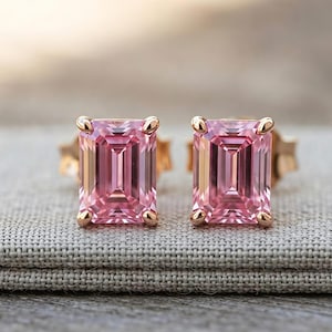 Op de afbeelding: Een paar oorknopjes met smaragdgeslepen roze edelstenen gezet in roségoudkleurig metaal. Elke rechthoekige steen wordt vastgehouden door vier kleine pootjes op de hoeken en heeft een gefacetteerd oppervlak dat het licht helder weerkaatst.