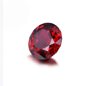 Può includere: Una gemma sfaccettata, di forma ovale, di colore rosso intenso. La gemma ha un taglio brillante, che riflette la luce e crea un effetto scintillante. La gemma è posta su uno sfondo bianco, evidenziando il suo colore e la sua chiarezza.