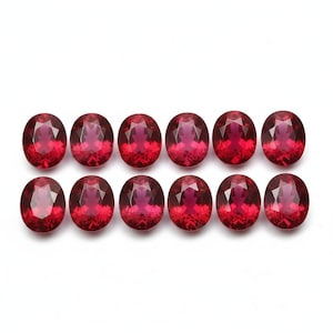 May include: Twelve oval-cut, deep red gemstones are arranged in two rows against a white background. The gems have a faceted surface that reflects light, creating a sparkling effect. The stones are of similar size and shape.