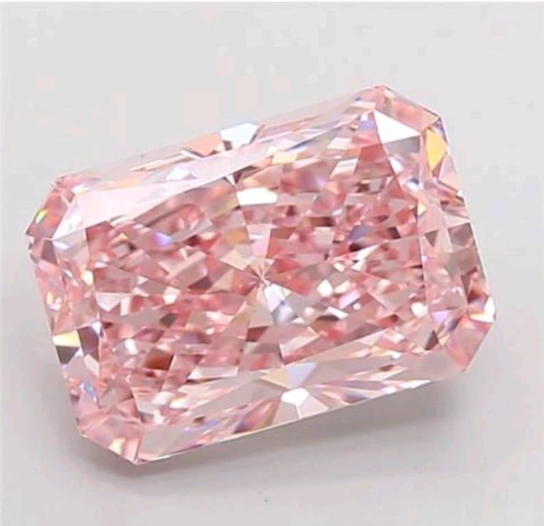 K&ouml;nnte beinhalten: Ein pinkfarbener Diamant im Radiant-Schliff mit rechteckiger Form und abgeschnittenen Ecken. Der Edelstein hat viele Facetten, die das Licht reflektieren und einen funkelnden Effekt erzeugen. Die Farbe ist ein zartes Rosa.