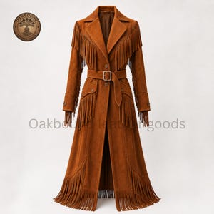May include: A long, brown suede coat featuring a notched lapel, a belted waist with a rectangular buckle, and long fringe detailing along the chest, sleeves, and hem. The garment includes buttoned cuffs and pockets, with the text Oakbound Leather Goods.