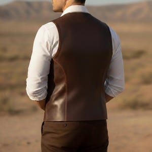 May include: A brown leather vest with a tailored fit, worn over a white dress shirt. The vest has a classic design with a smooth, polished finish. The image is taken outdoors with a desert landscape in the background.