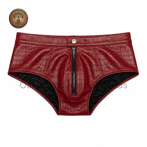 May include: Red faux leather shorts with a crocodile texture. The shorts have a black zipper down the front and a button closure at the top. The interior is lined with black fabric. The shorts are a low-rise style.