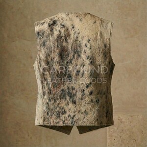 May include: A vest made of cowhide with a natural pattern of beige, brown, and black spots. The back of the vest is visible, with the text "CAREYON LEATHER GOODS" printed on it. The vest has a classic, tailored design.