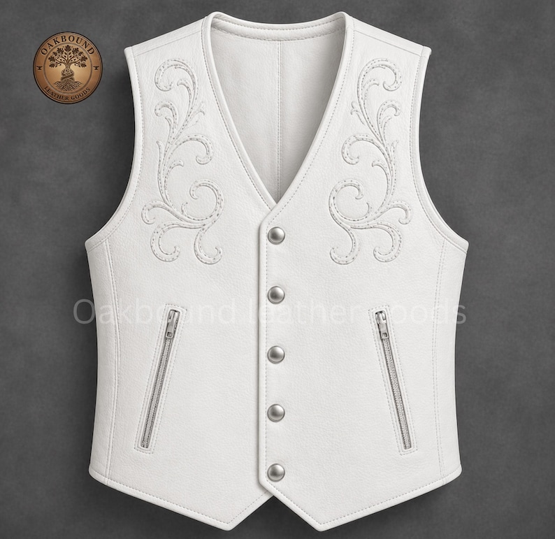 May include: A white leather vest with intricate embroidered floral designs on the front. The vest features a V-neck, silver-toned buttons, and two zippered pockets. The brand name "Oakbound Leather Goods" is visible on the upper left.
