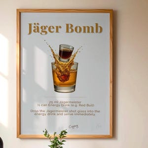 Puede incluir: Un cartel enmarcado con el texto "Jäger Bomb" en letras doradas. La imagen muestra un vaso de chupito de líquido oscuro cayendo en un vaso de líquido ámbar, creando un chapoteo. El cartel incluye instrucciones.