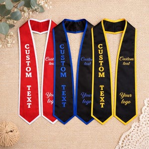 May include: Four graduation stoles in red, black, and gold. Each stole has the words "CUSTOM TEXT" embroidered in a contrasting colour. The stoles also feature the words "Your logo" and "Custom text".