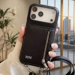 May include: Black leather phone case with a wallet and zipper closure. The case has a strap and the initials "MM" are embossed on the front. The phone case is shown with a phone with three camera lenses.