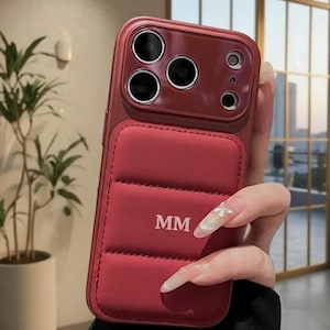 以下が含まれることがあります： 赤色の電話ケース。キルティングのデザインと、白で「MM」のイニシャルが入っています。ケースには複数のレンズを備えたカメラモジュールがあります。このケースは、携帯電話を保護し、スタイリッシュな外観を追加するように設計されています。