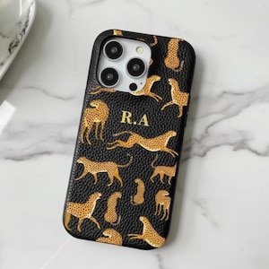 May include: Black phone case with a cheetah print design. The case features a repeating pattern of cheetahs in various poses, with gold accents. The initials "R.A" are displayed in gold. The case is designed for a smartphone.