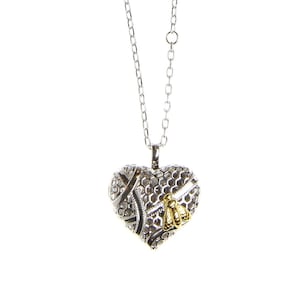May include: Silver necklace with a heart-shaped pendant. The pendant has a honeycomb design and a gold-coloured bee accent. The necklace hangs on a delicate chain, creating a charming and detailed piece of jewellery.